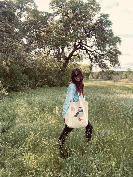 Person carrying a cotton tote bag featuring a print of a painted puffin illustration and humorous definition