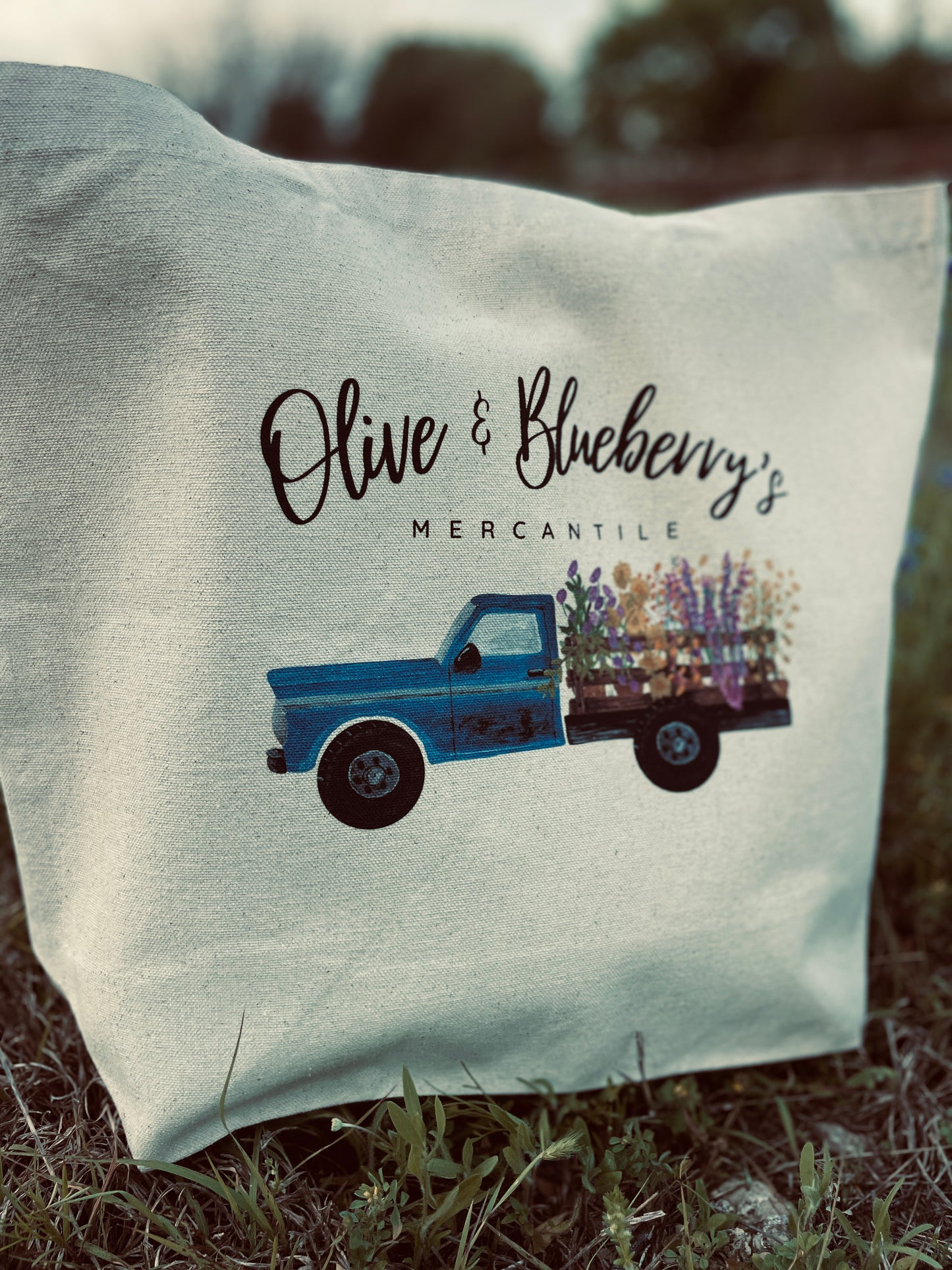 Back view of cotton canvas tote bag with Olive and Blueberry's Mercantile blue farm truck logo and flowers