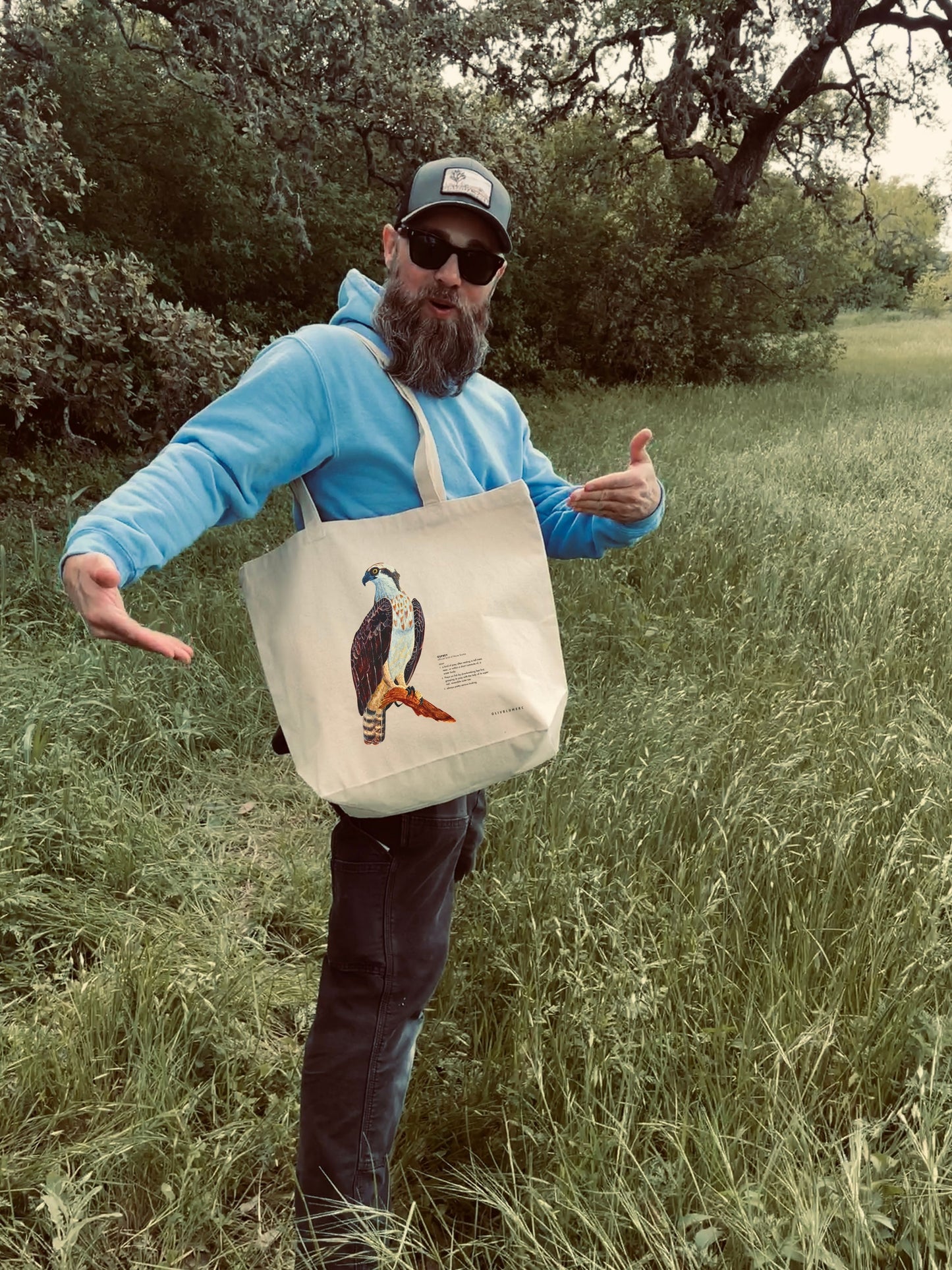 Person carrying a cotton tote bag featuring a print of a painted osprey illustration and humorous definition