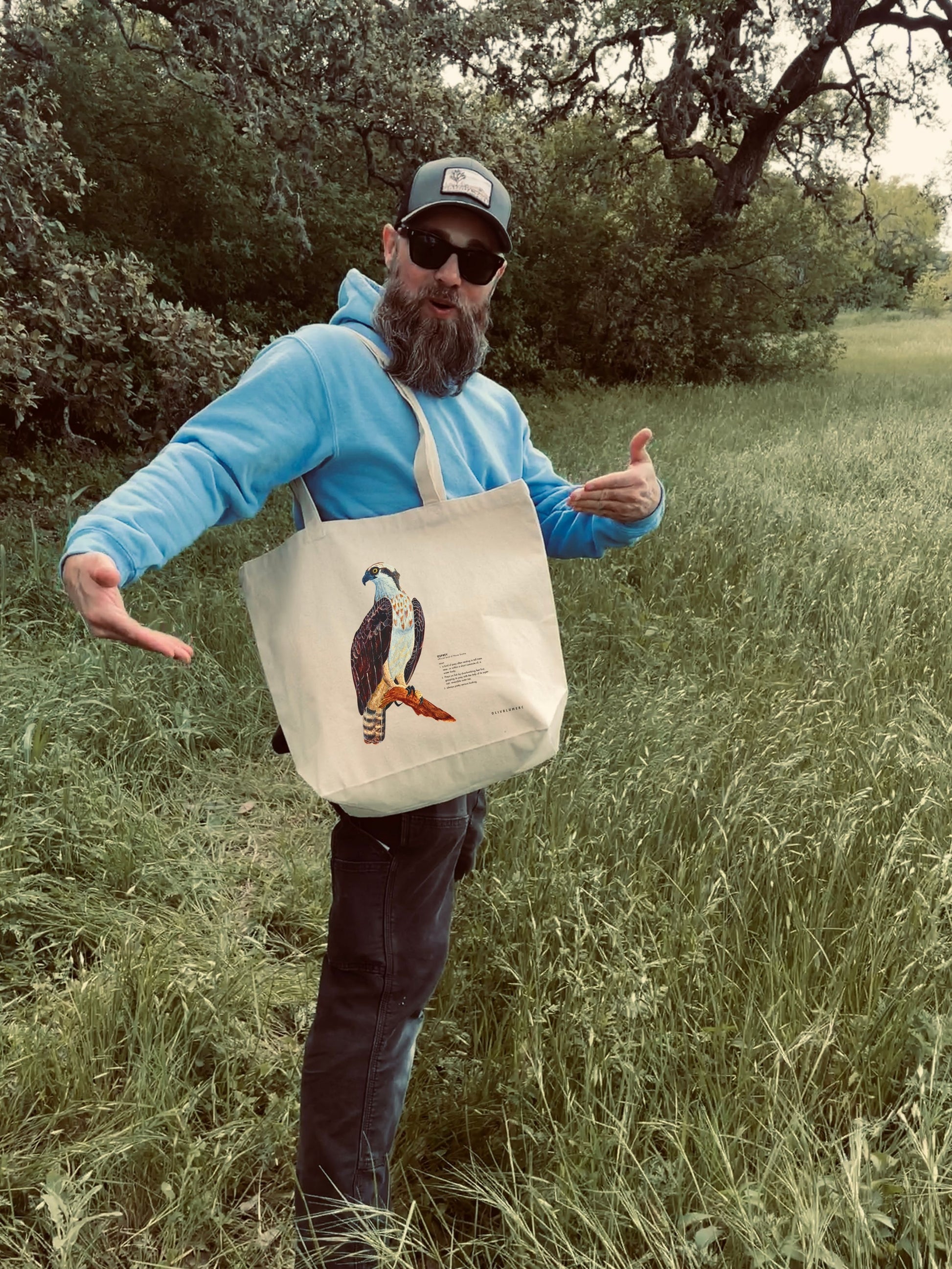 Person carrying a cotton tote bag featuring a print of a painted osprey illustration and humorous definition